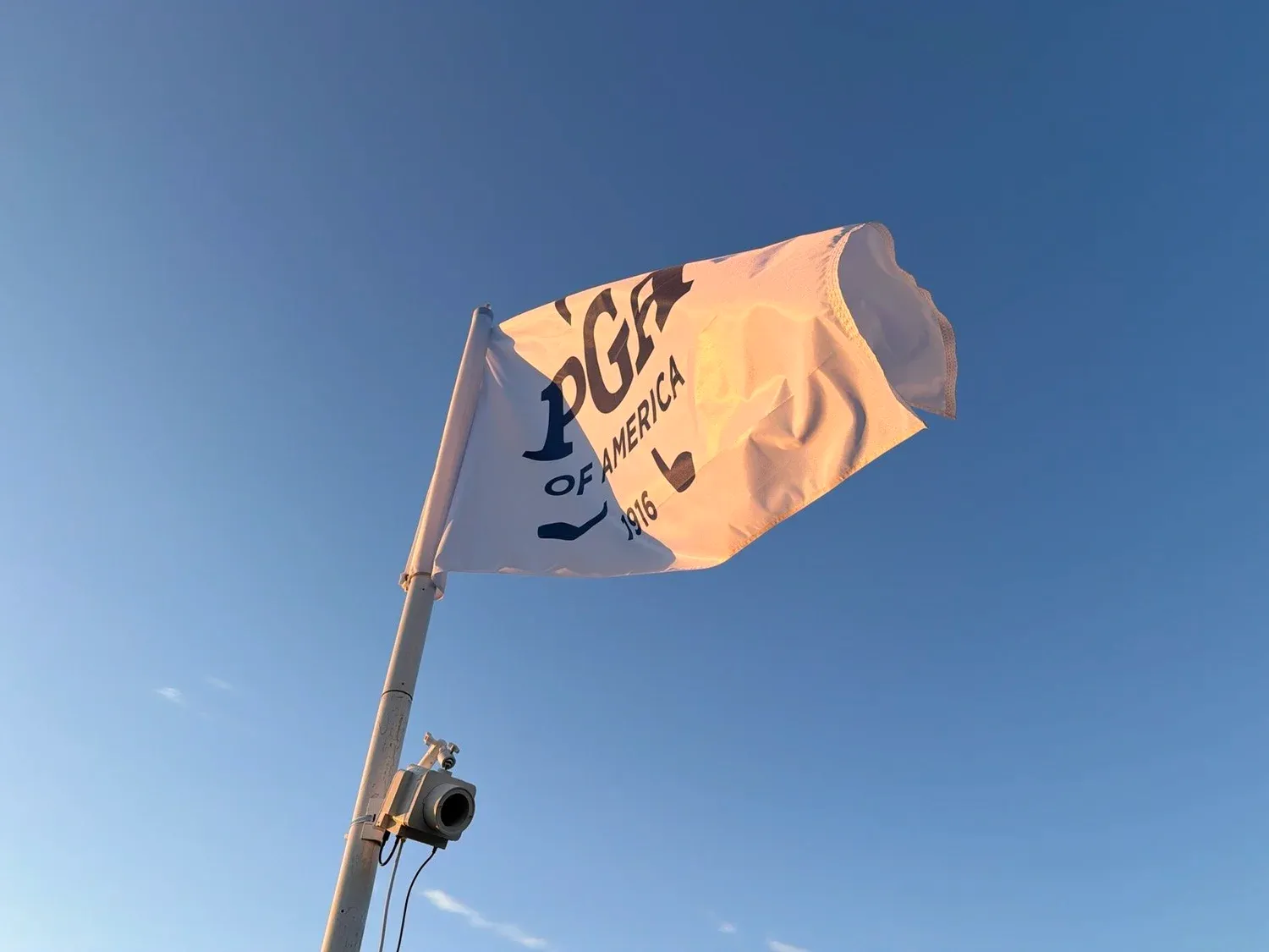 A Queues sensor mounted on a PGA of America flagpole against a blue sky