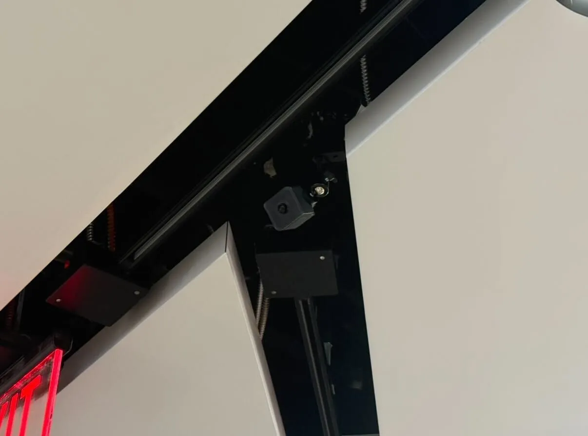 A black Queues sensor mounted on a black ceiling rail, blending into the structure